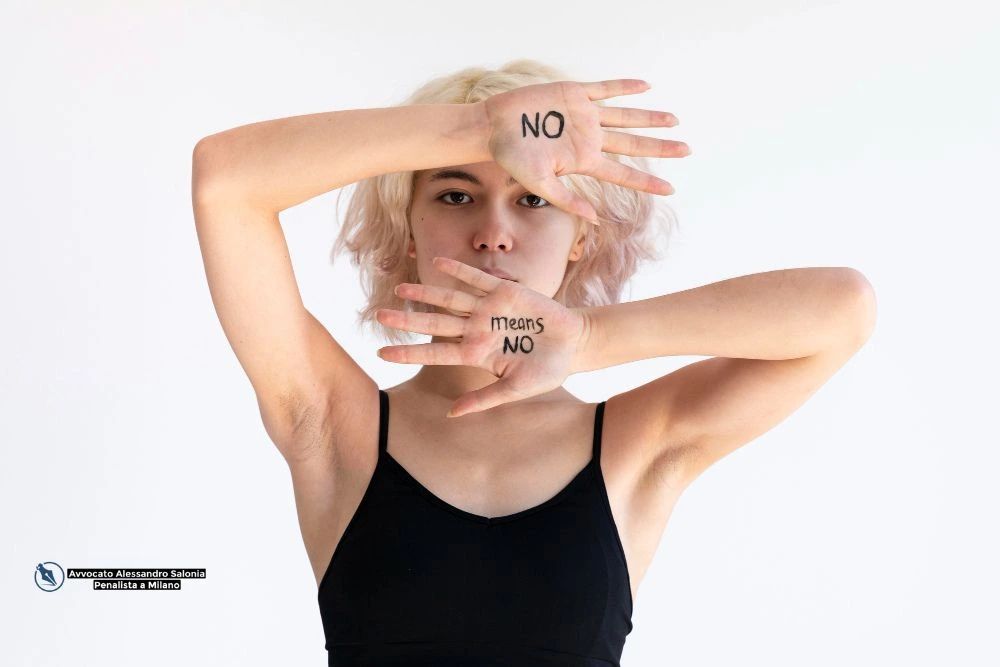 Una giovane donna si protegge il volto con le mani, sulle quali è scritto "NO means NO", a simboleggiare il rifiuto della violenza psicologica e del body shaming. L'immagine rappresenta la tutela legale per il reato di maltrattamenti in famiglia, con il logo dello Studio dell'Avvocato Penalista Alessandro Salonia a Milano.